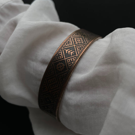 Brass bracelet on a white sleeve against a black background
